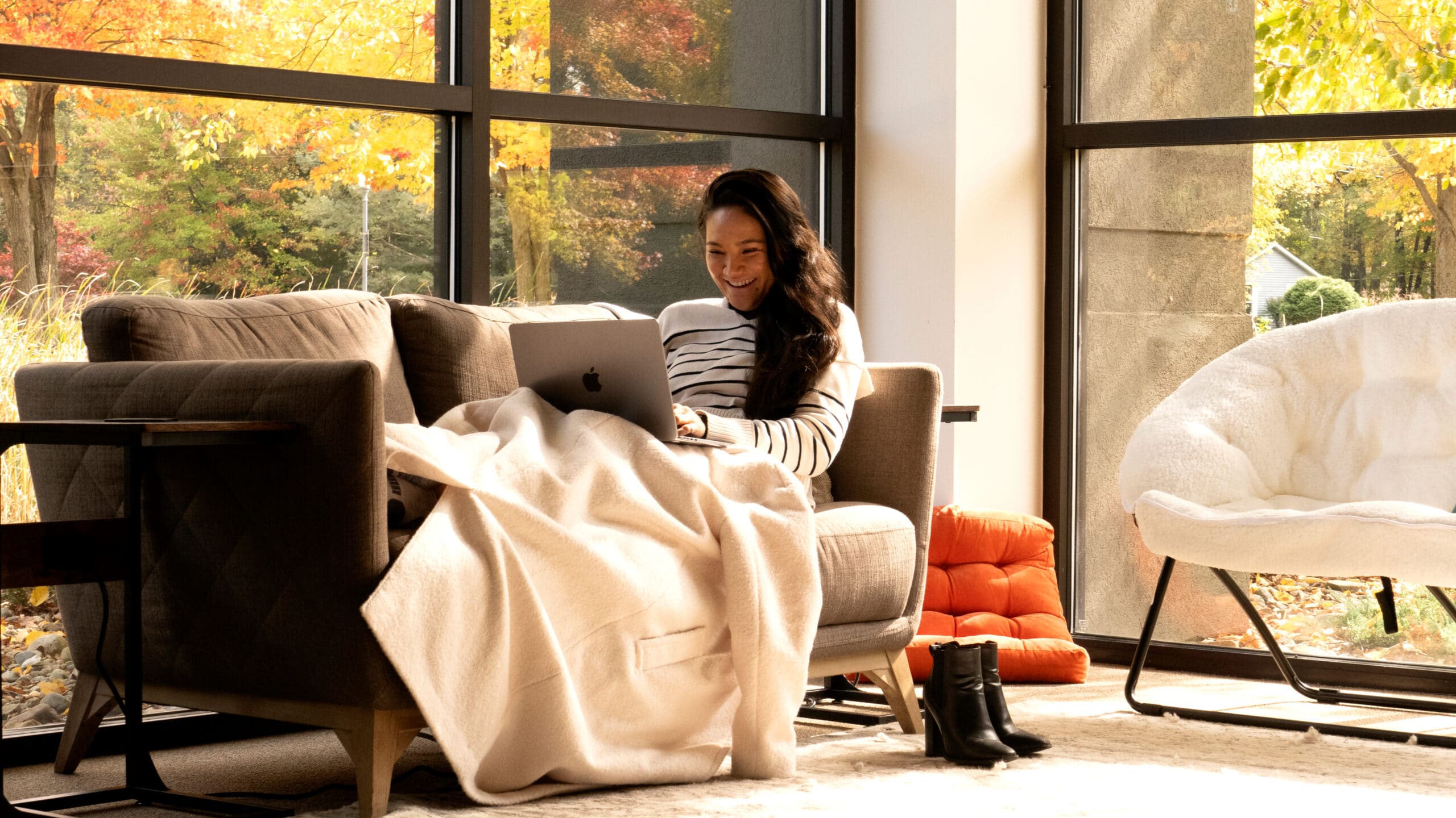A woman sitting on a couch, smiling and looking at her computer